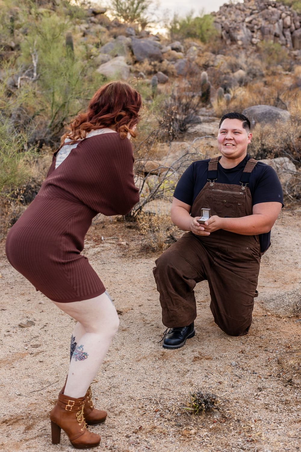 A proposal moment captured in a desert landscape with rocky terrain and desert plants.