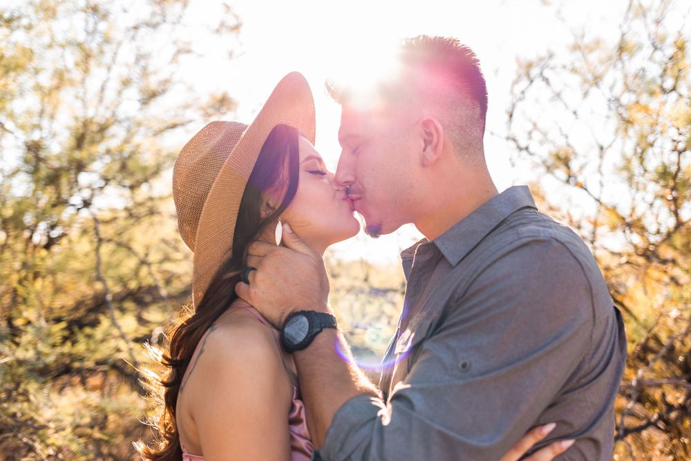 Romantic couple sharing an intimate moment at sunset with sunflare and desert landscape in background.