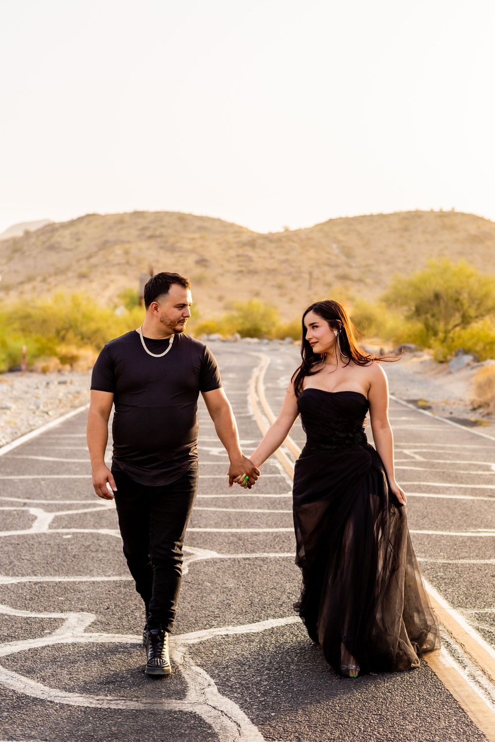 Couple walking hand in hand on patterned road in desert landscape.