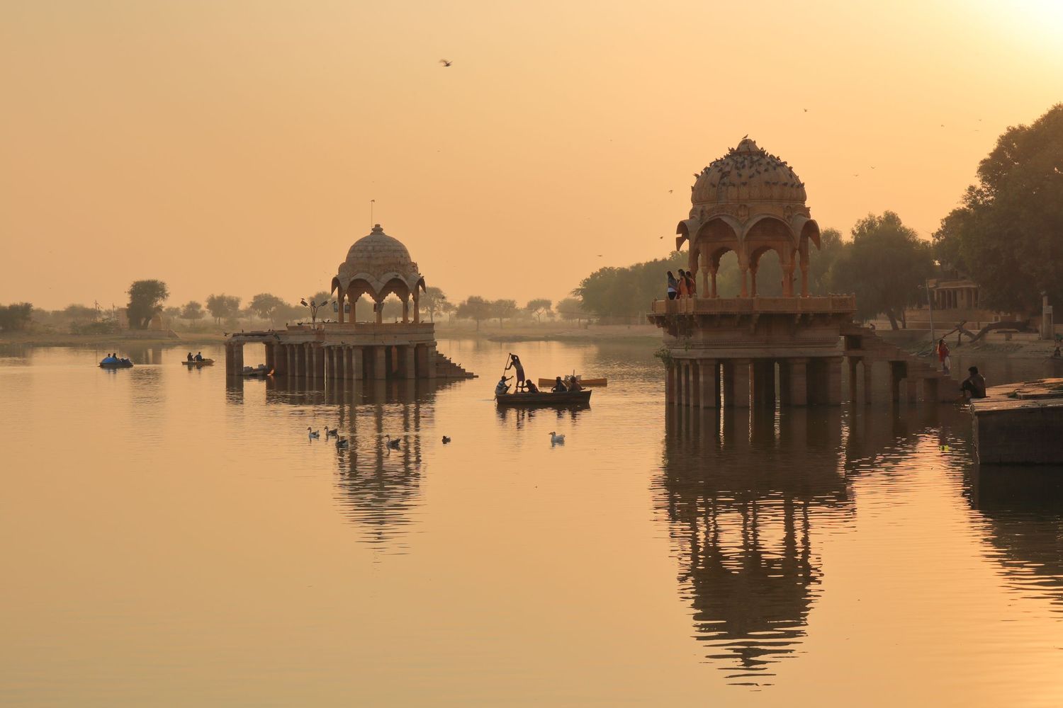 Sunset over lake with traditional Indian pavilions reflected in calm waters.