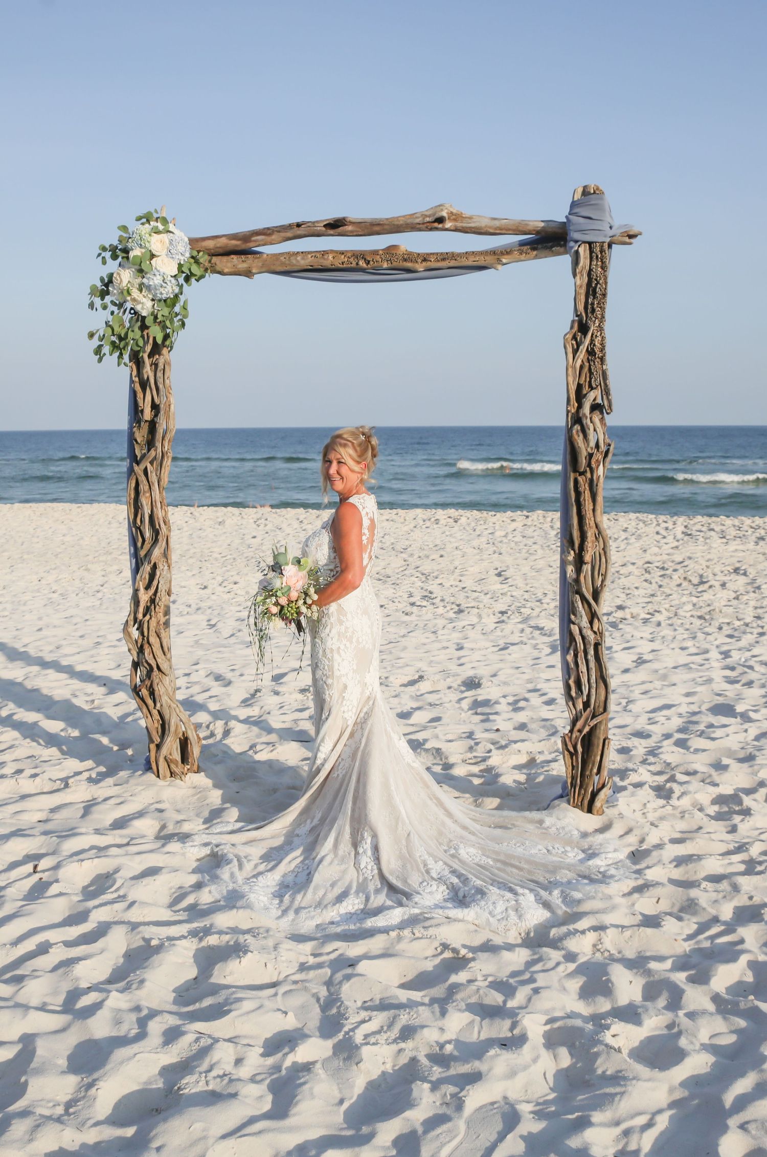 Beautiful beach wedding arch made of driftwood and flowers frames a scenic ocean view.