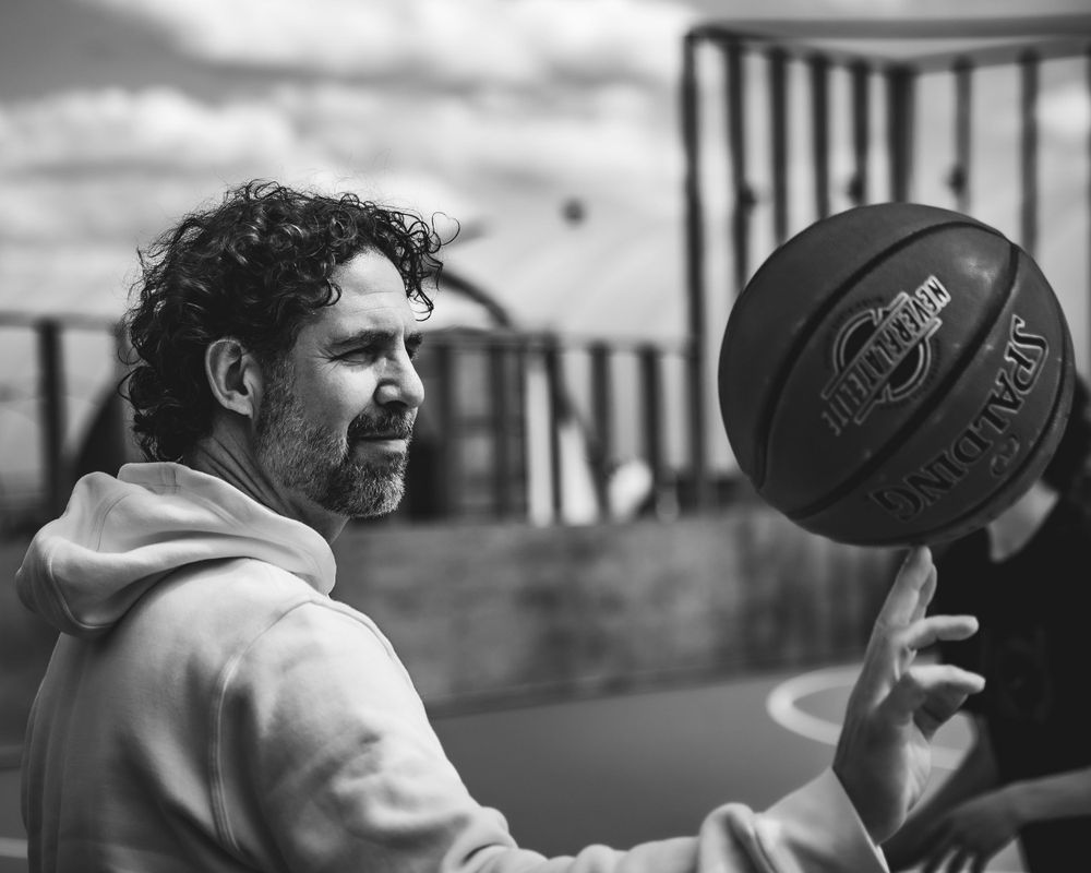Person spinning a basketball in black and white portrait against cloudy sky.