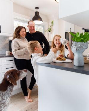 A family shares a lighthearted moment in their kitchen with their German Shorthaired Pointer dog.