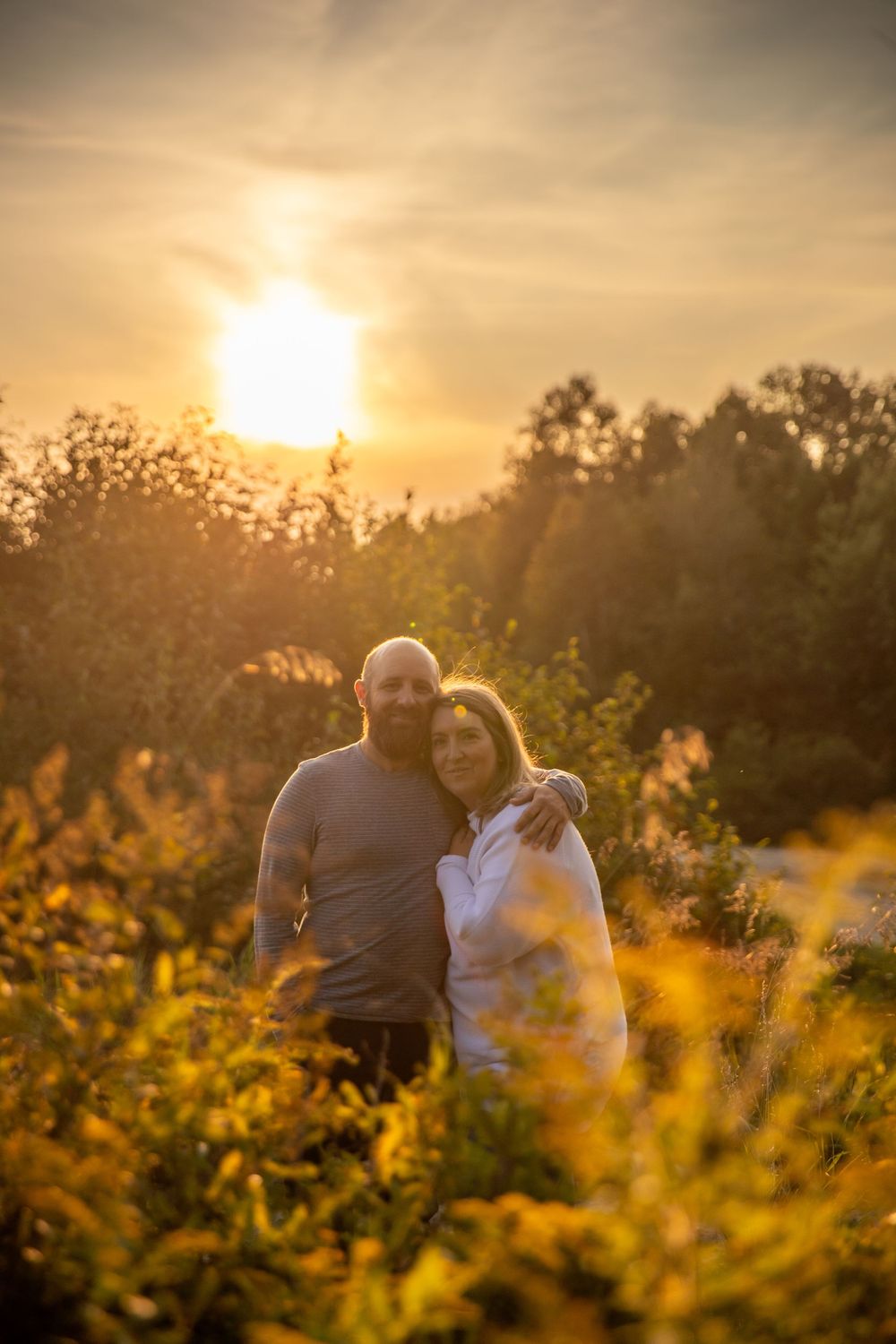 Couple embracing in golden sunset light among wildflowers in a field.