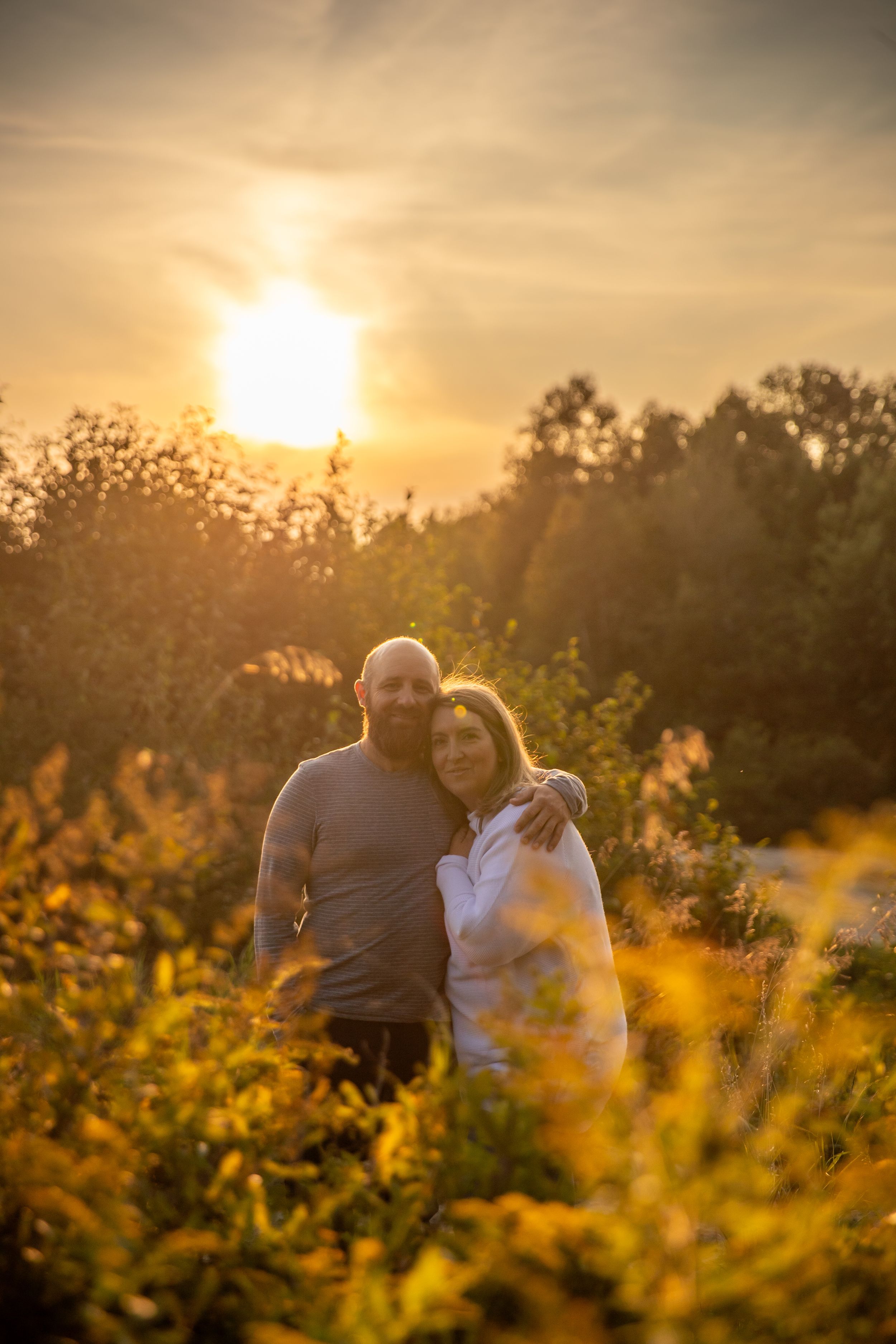 Couple embracing in golden sunset light among wildflowers in a field.
