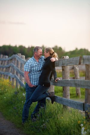A couple embraces by a rustic wooden fence at golden hour in the countryside.