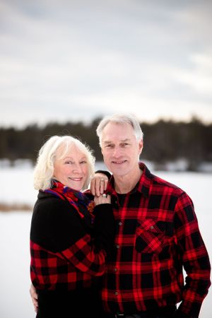 A couple wearing coordinating red and black buffalo plaid flannel poses together in a snowy winter setting.