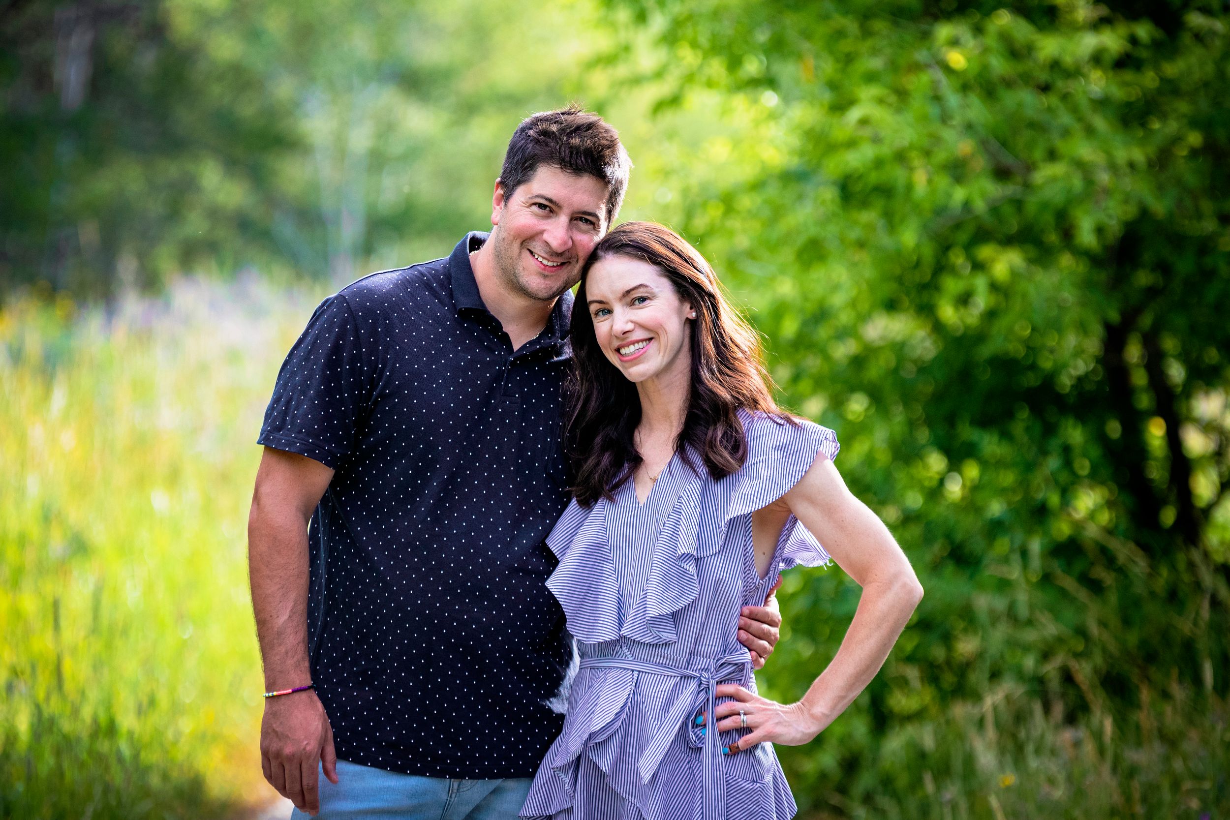 A couple poses outdoors with lush green foliage in the background.