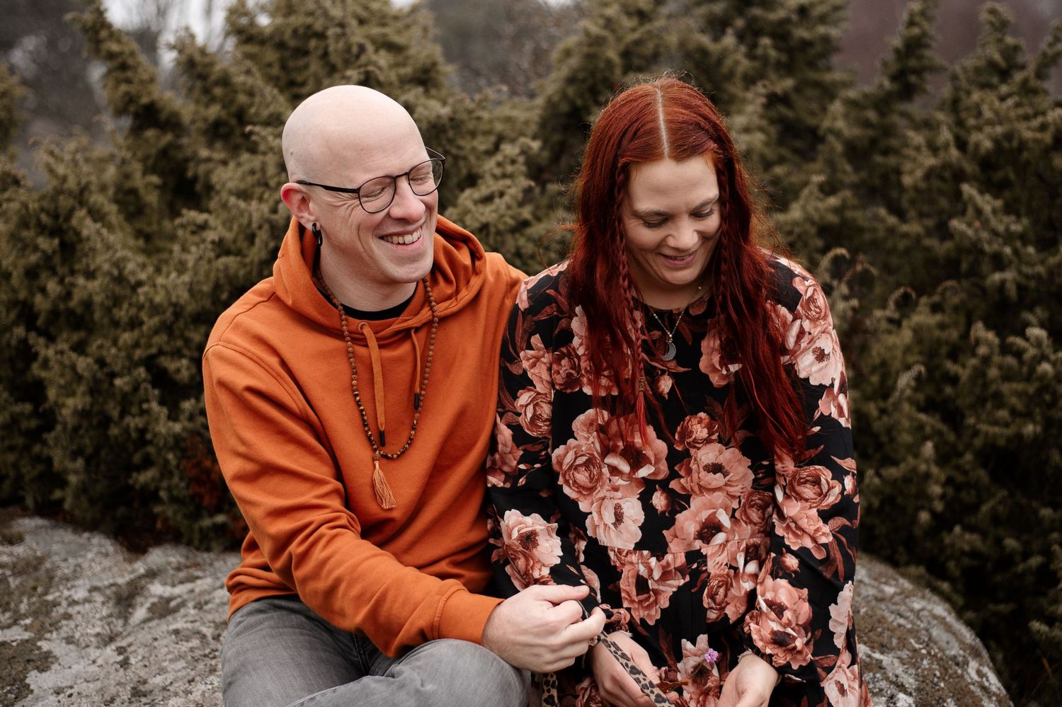 Couple sharing a laugh while sitting on rocks with evergreen trees in background.