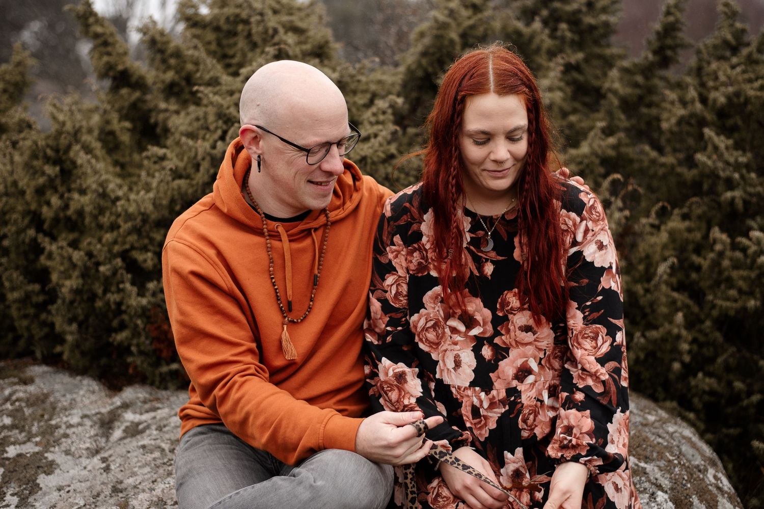 Couple sitting on rocky outcrop wearing orange hoodie and floral dress.