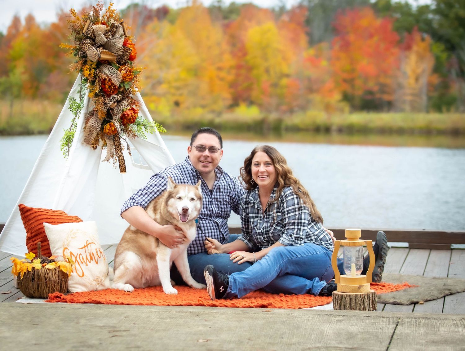 Autumn lakeside photo setup with teepee decor, dog, and colorful fall foliage in background.