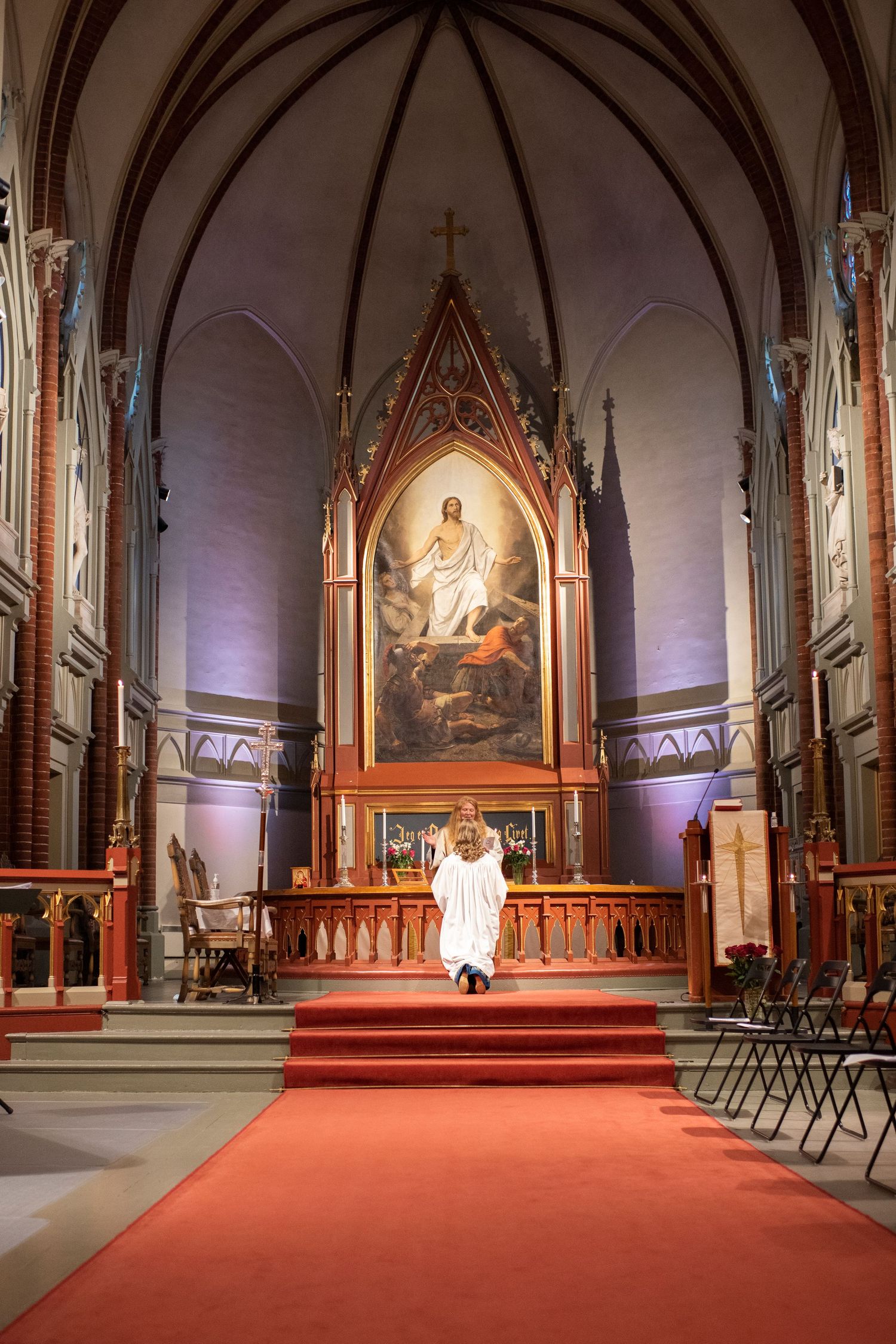Interior of a Gothic church with a red carpet leading to an altar featuring a large religious painting.