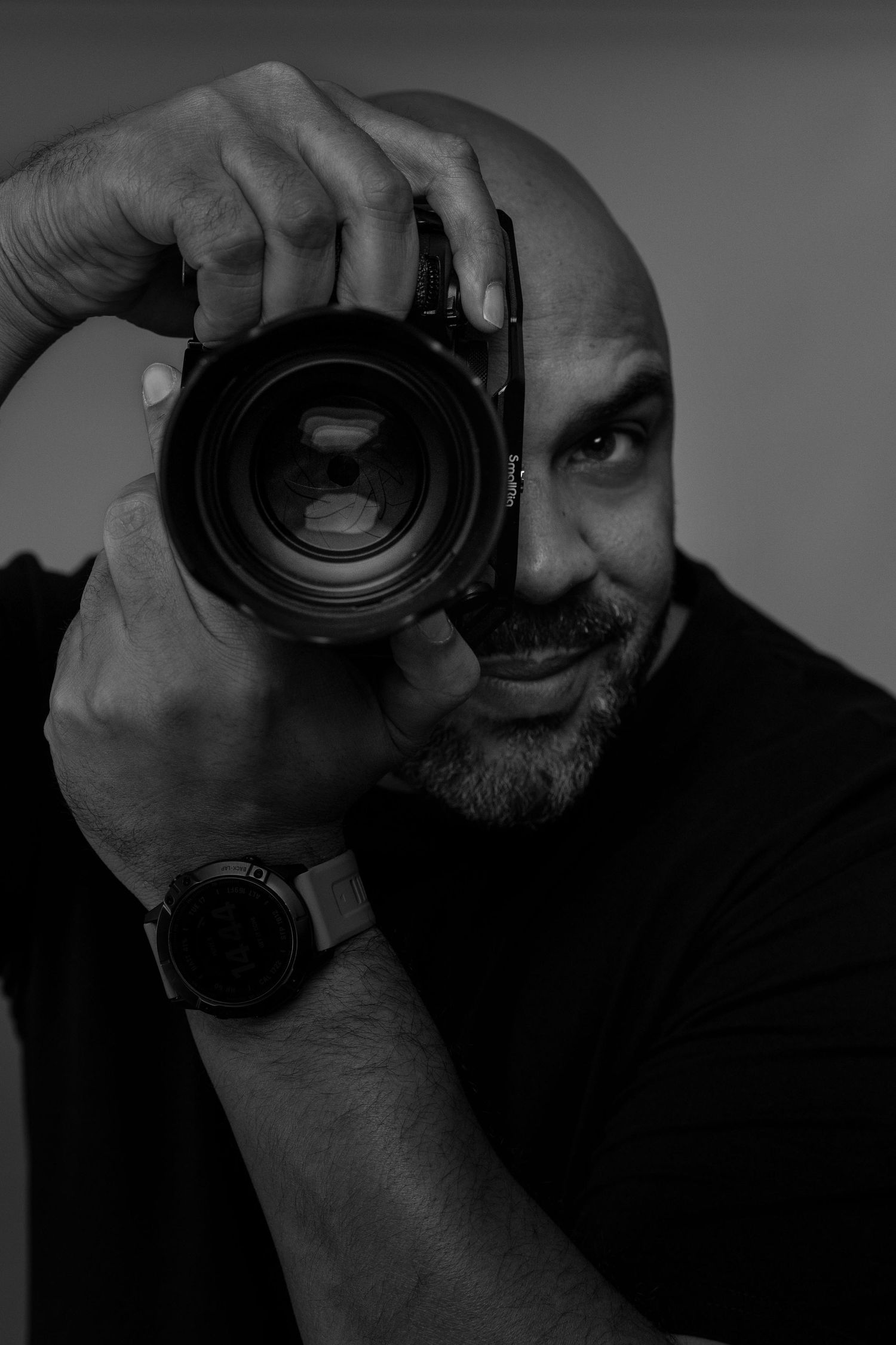 Black and white portrait of photographer holding professional camera in front of face.