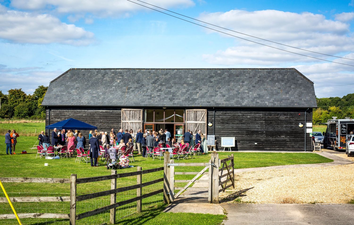 Rustic barn wedding venue exterior with wooden fencing and gravel path on a sunny day.