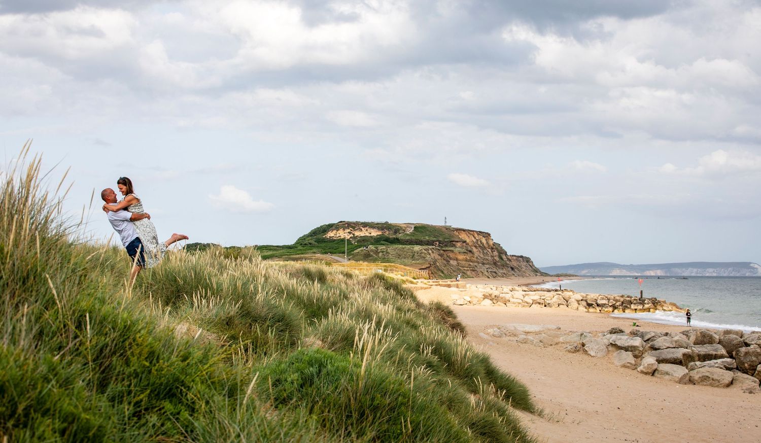Scenic beach landscape with sand dunes and coastal cliffs under dramatic cloudy skies.