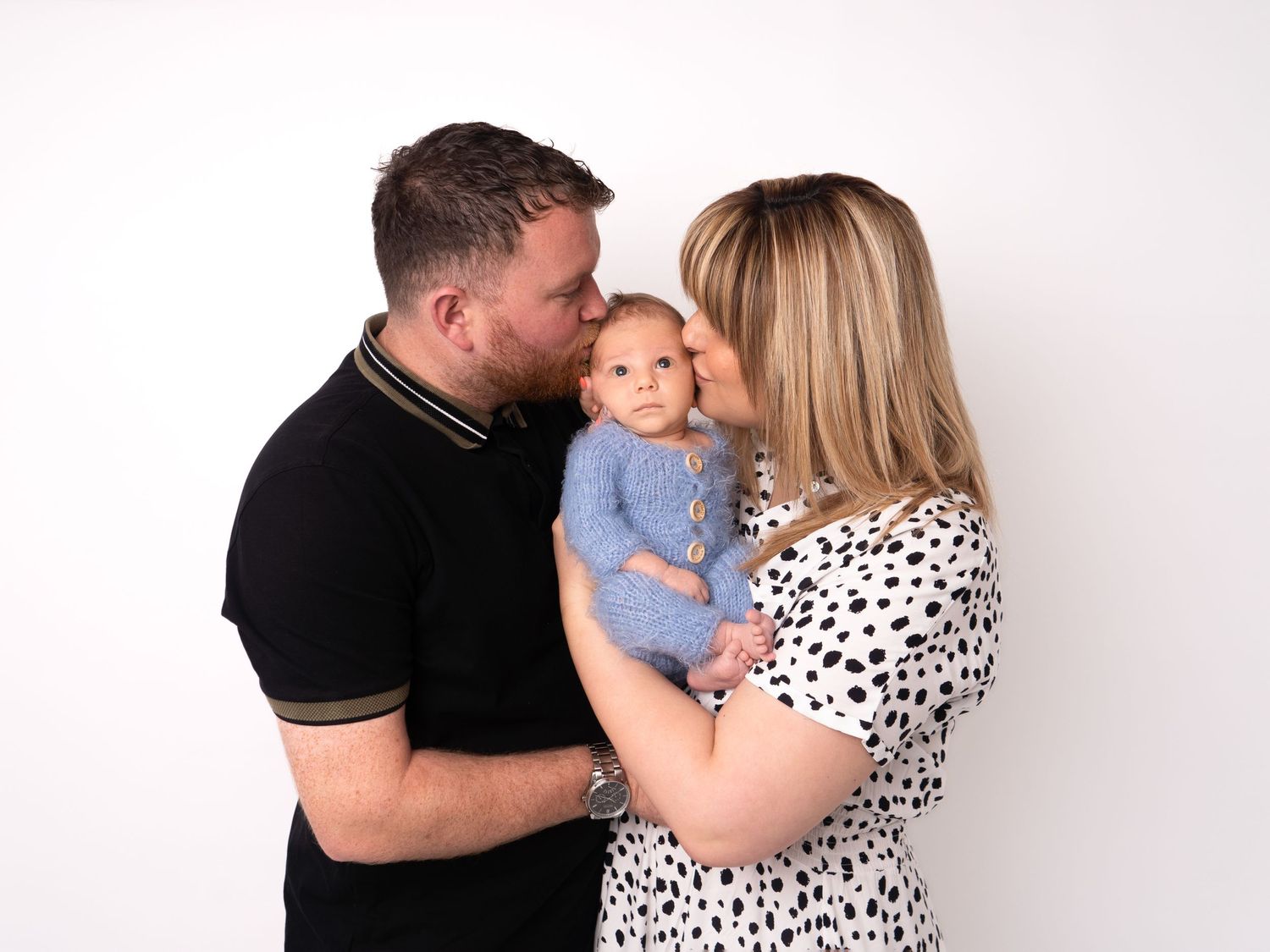 mother and father holding newborn baby in blue fluffy romper at newborn photoshoot in Doncaster.