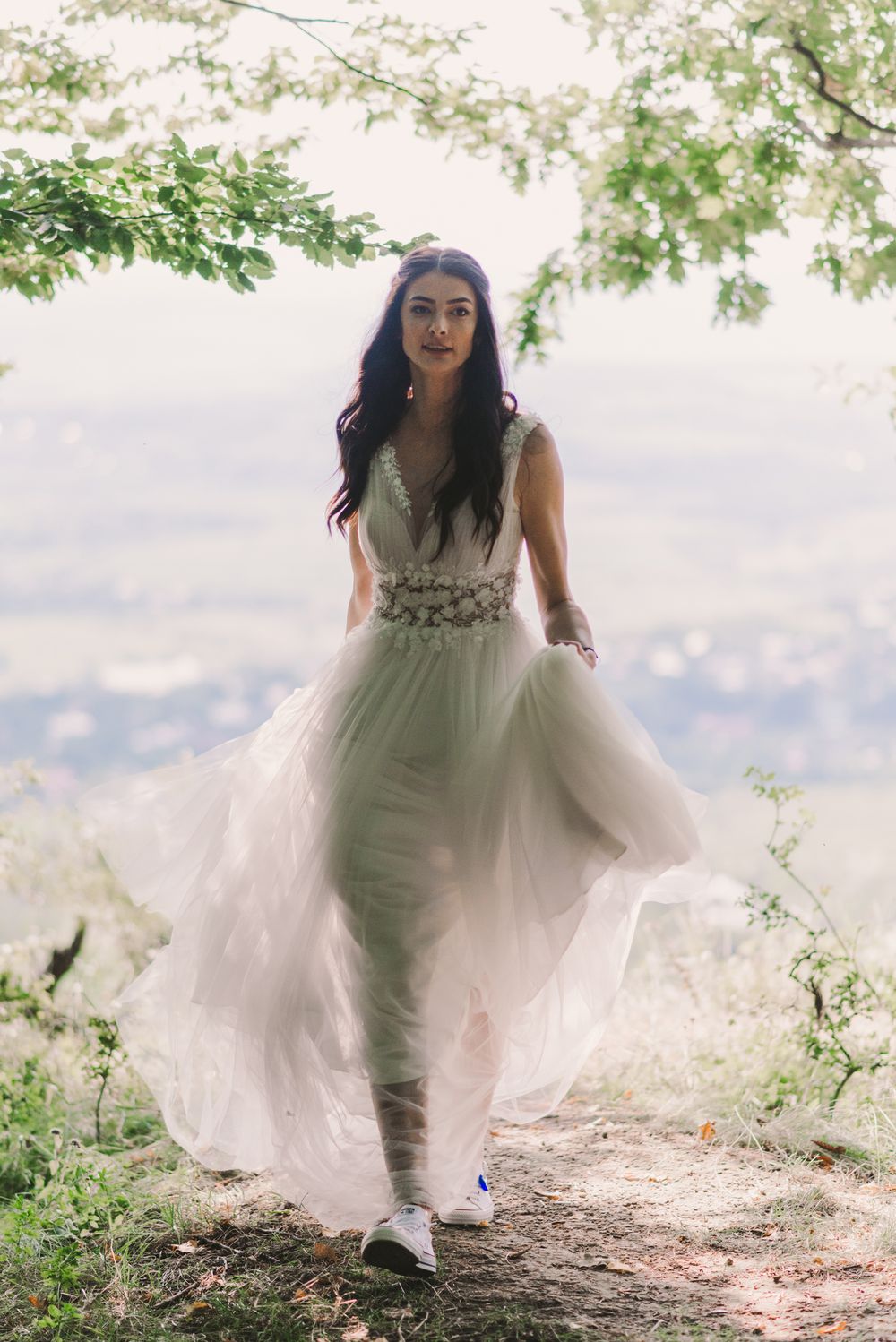 Bride in a flowing white dress playfully walks along a scenic mountain path.