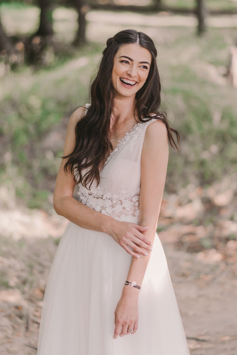 Bride in lace wedding dress laughs joyfully during outdoor photo session.