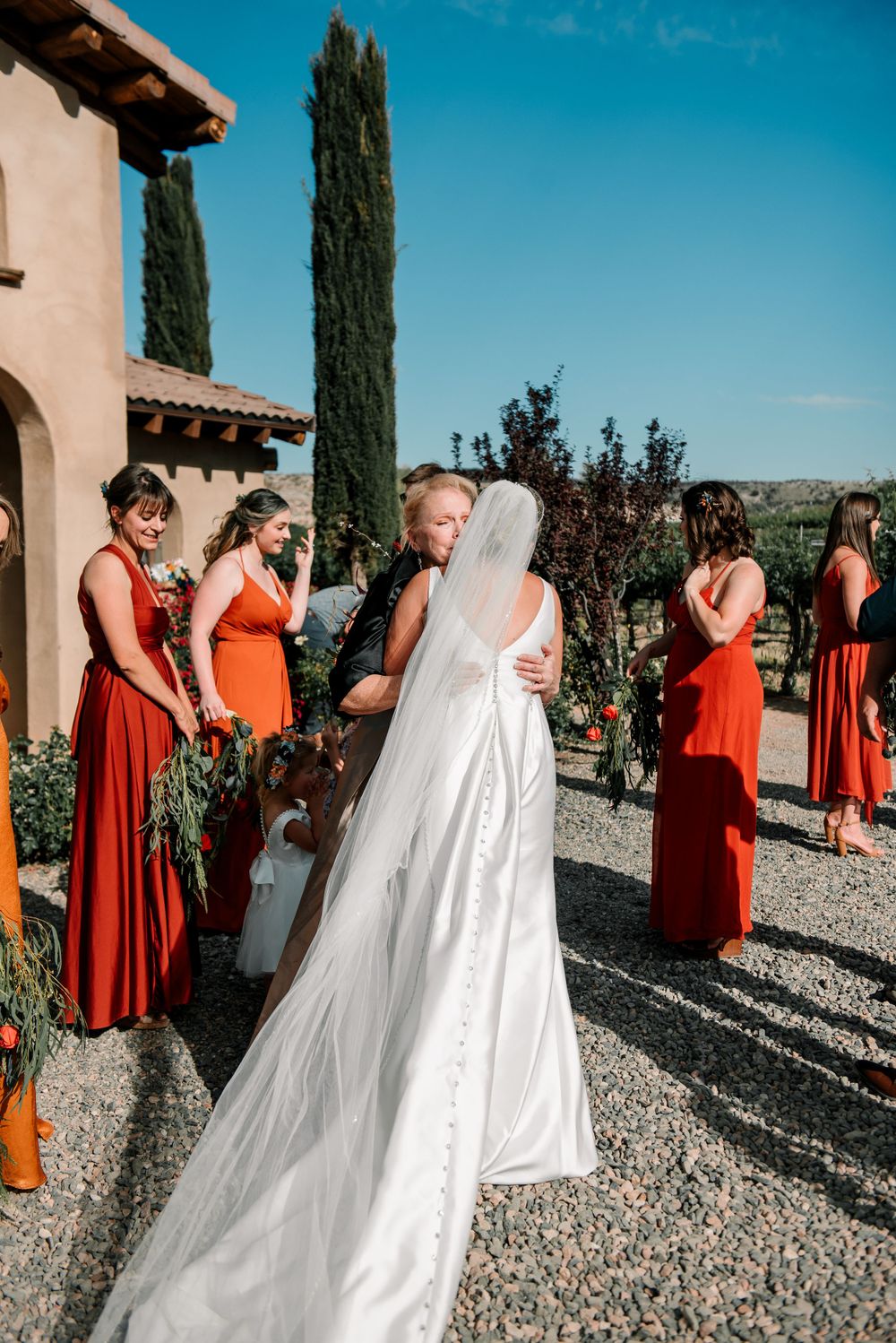 Wedding party in burnt orange bridesmaid dresses gathered outside Mediterranean-style venue.