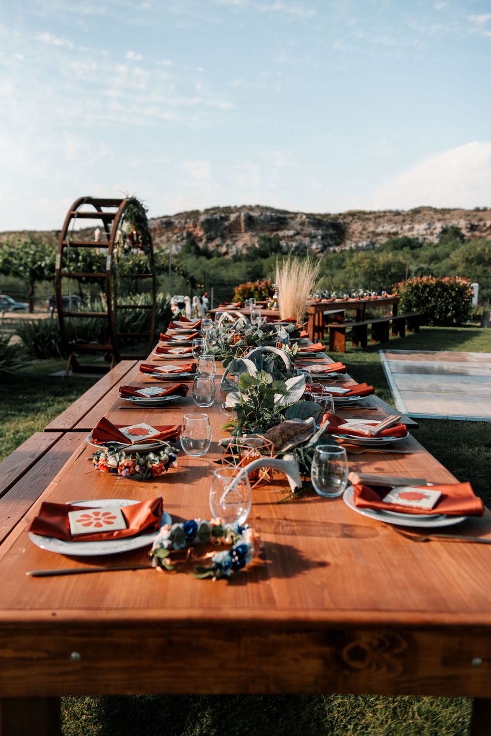 Elegant table settings with copper chargers and floral centerpieces at an outdoor vineyard wedding reception.