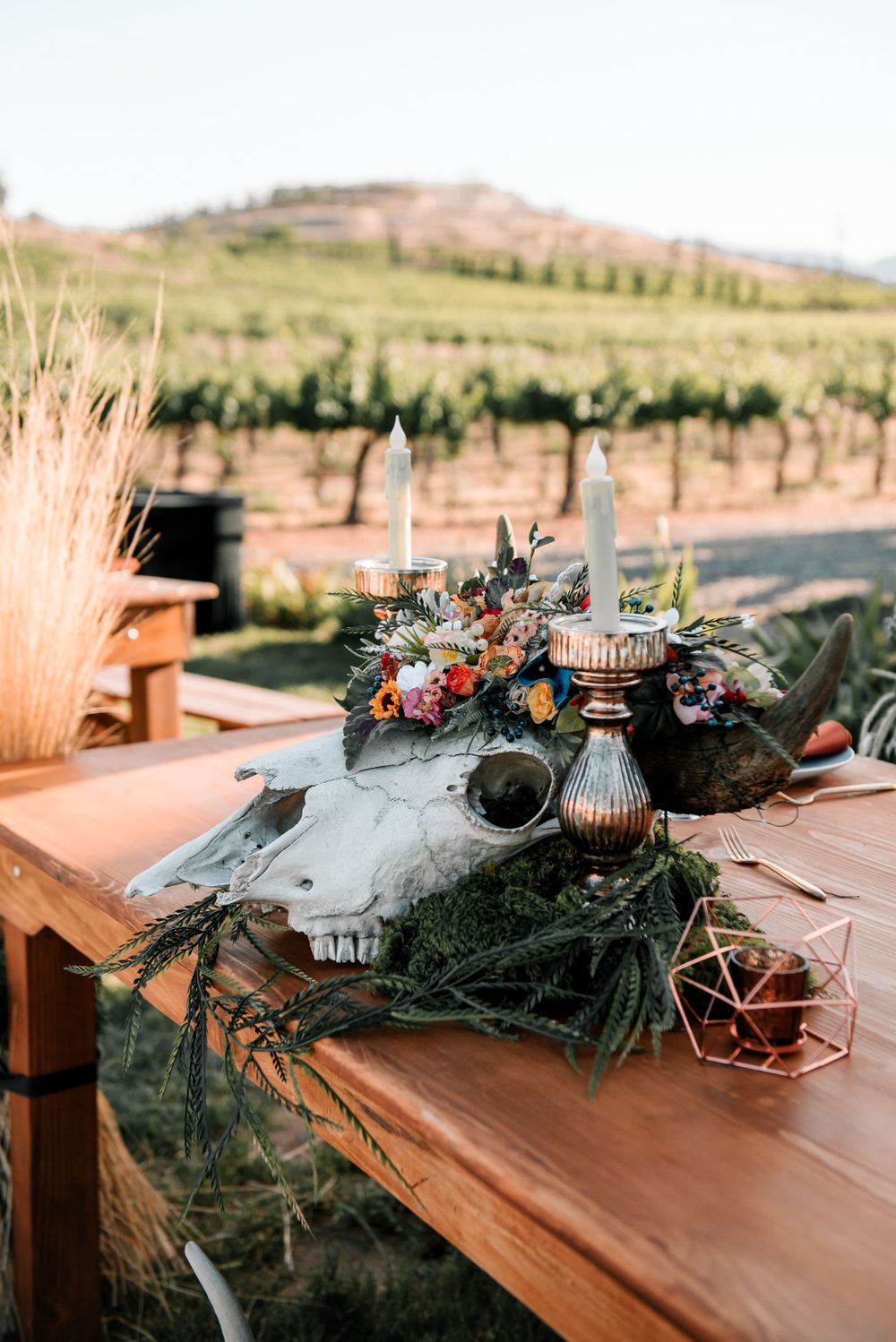 Rustic wooden table decorated with dark greenery and floral arrangements at an outdoor venue.