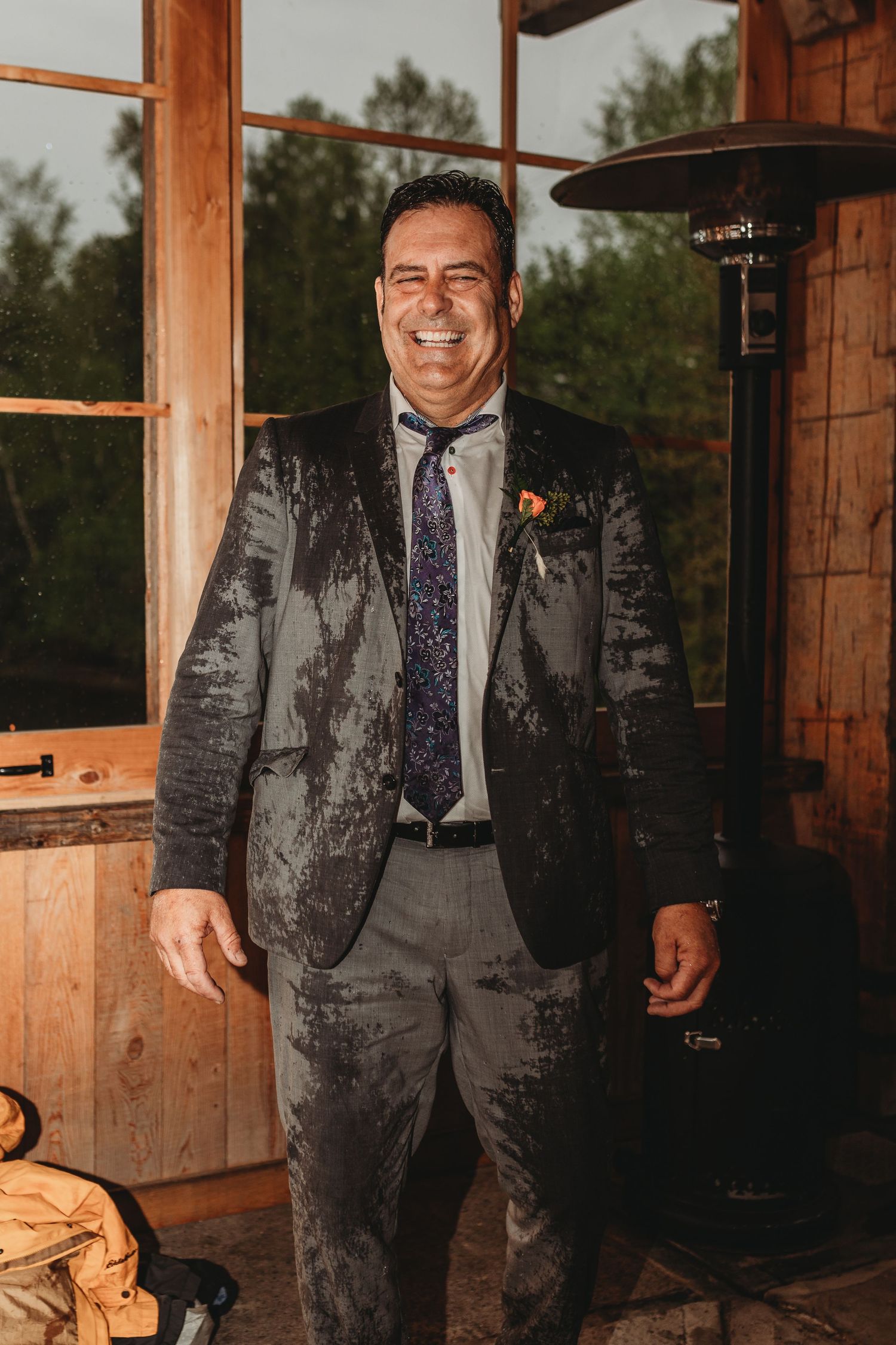Joyful guest in formal suit smiling inside rustic wooden venue.