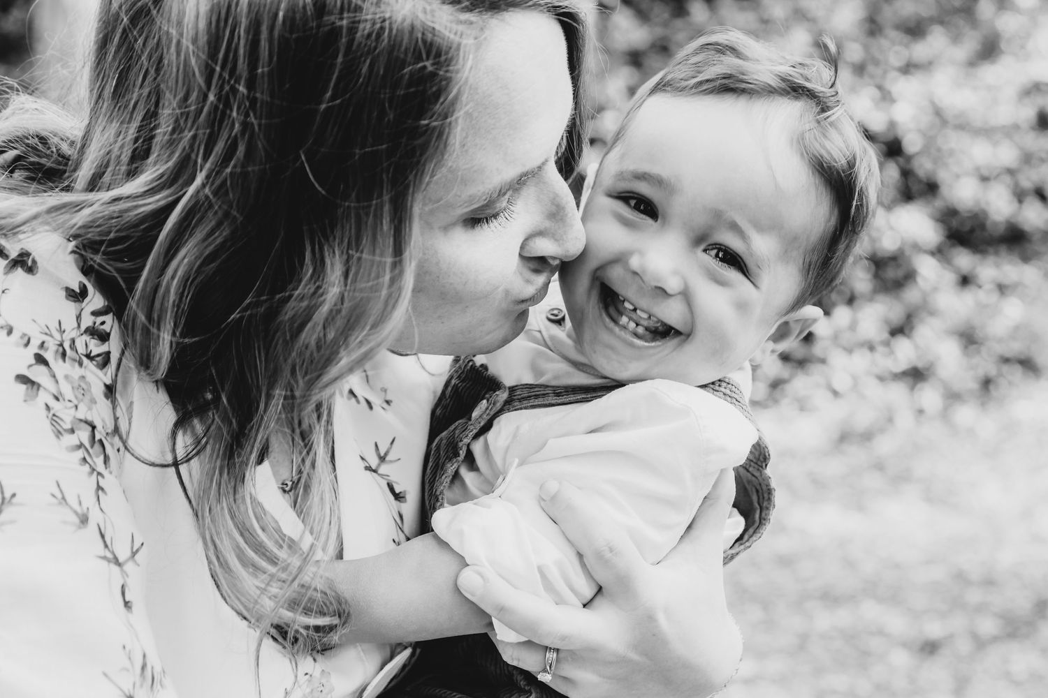 Black and white photo captures joyful interaction between mother and child outdoors, Highgate Woods, London.