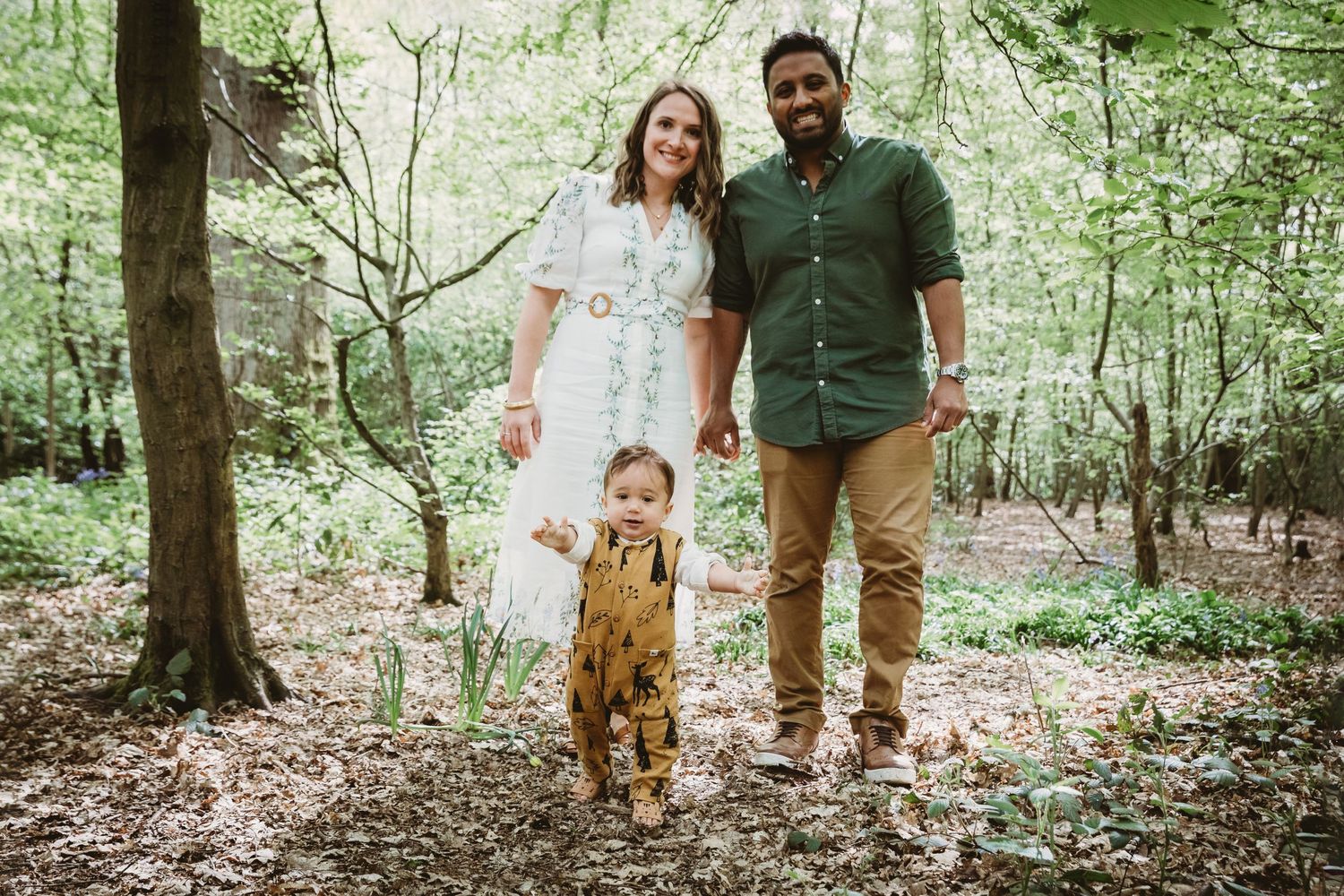 A family stands together in a lush forest setting wearing coordinated casual outfits, Highgate Woods, London.