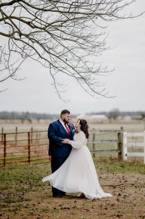 Bride and groom embracing under a tree during their windy January wedding.