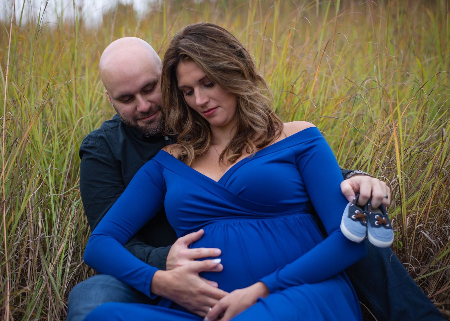 Intimate maternity portrait of couple sitting among tall grass in natural outdoor setting.