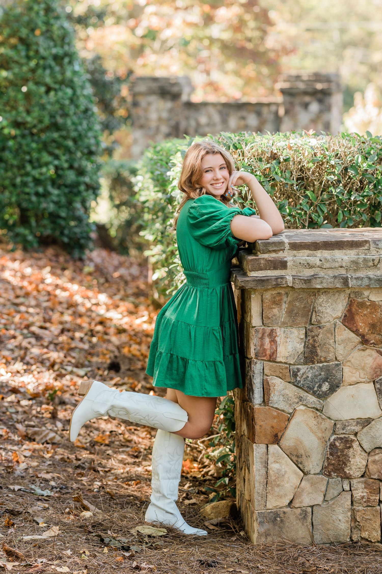 Green dress and white boots ensemble photographed near decorative stone wall in garden setting.