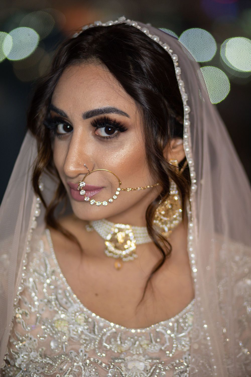 Traditional South Asian bride wearing an ornate white dress with detailed beadwork and jewelry including a nath nose chain.
