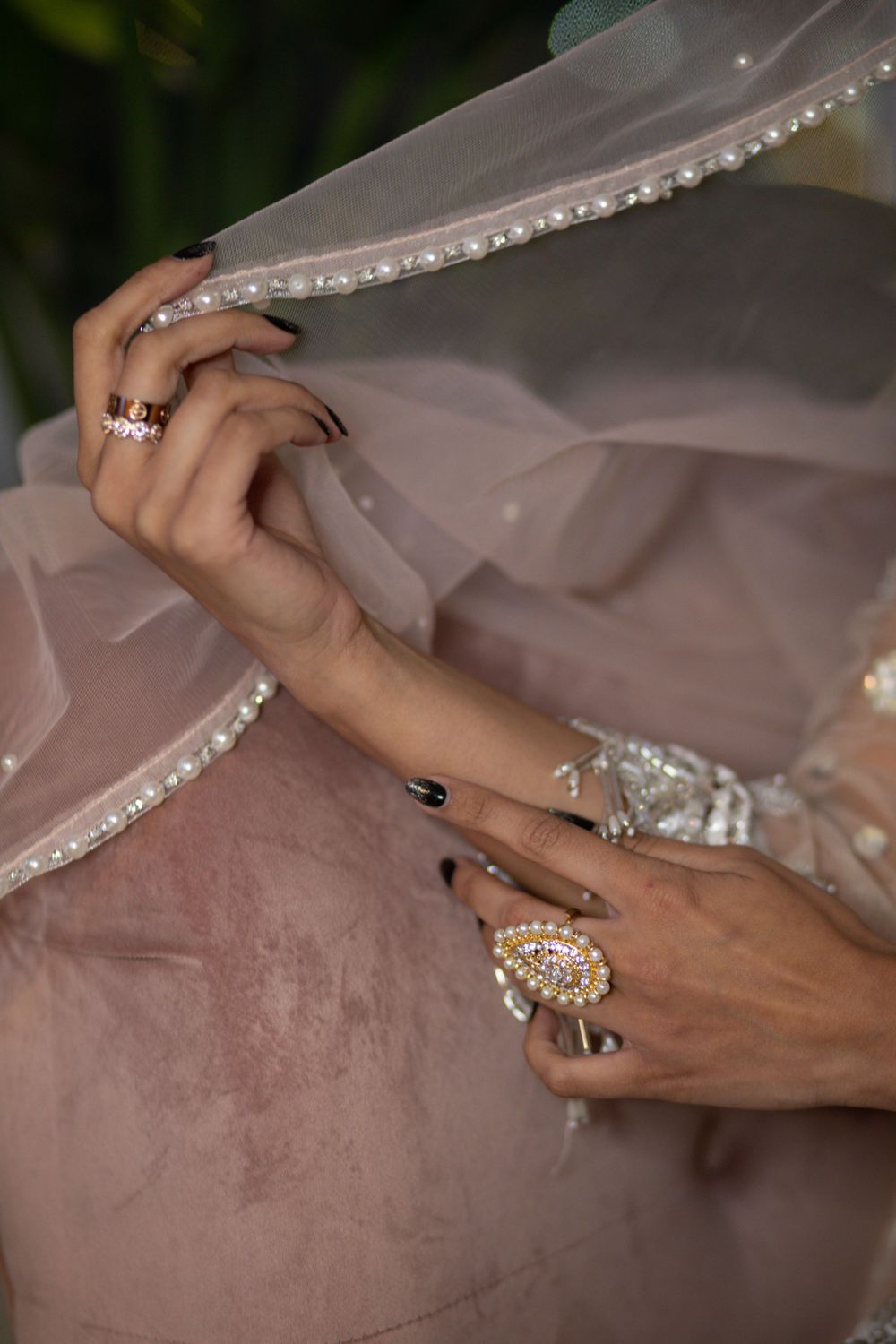 Close-up of hands holding a beaded veil, showing intricate rings and jewelry details.