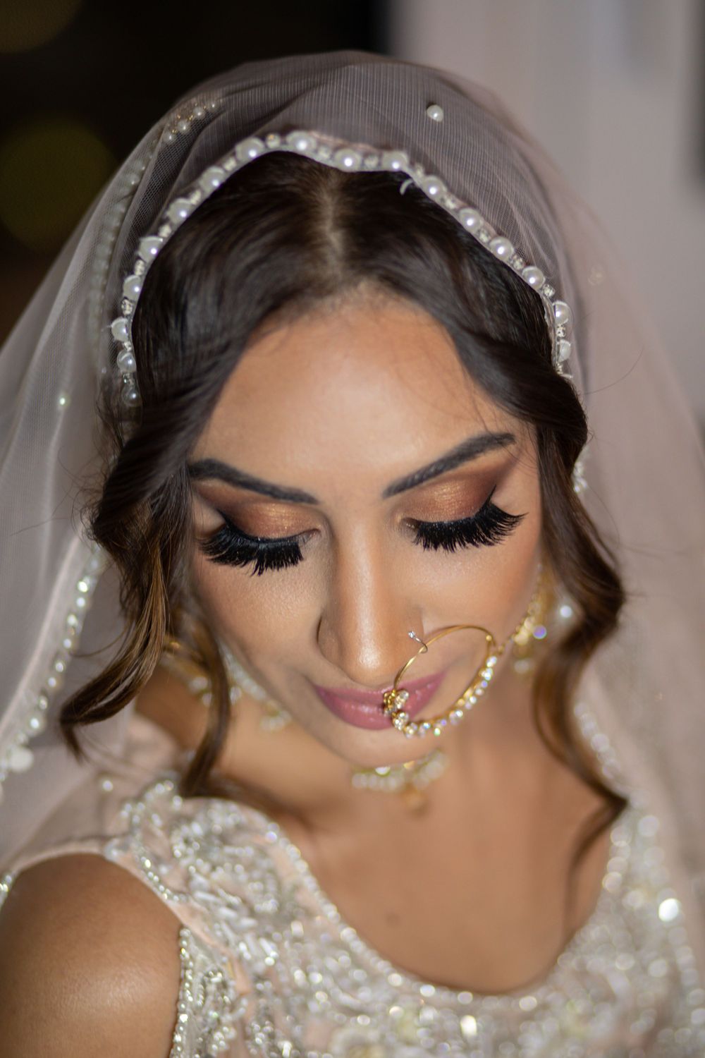 Detailed close-up of bridal makeup with long lashes, jeweled nose chain and crystal-trimmed veil.