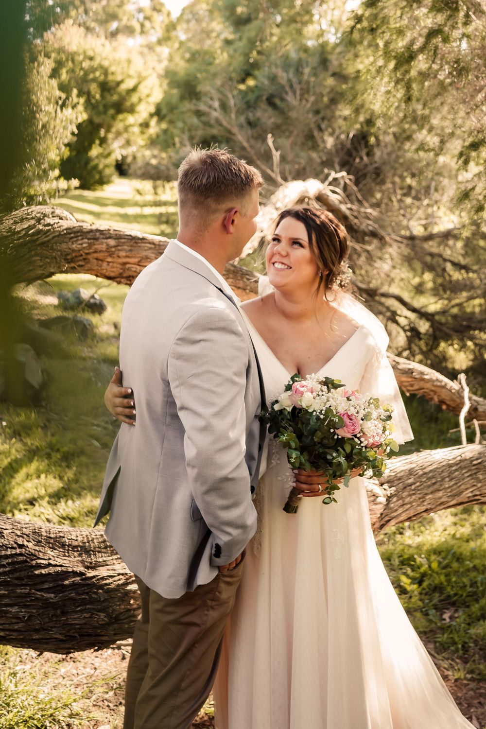 bride in blush dress holding pink bouquet shares a tender smile with groom in blue jacket and chinos