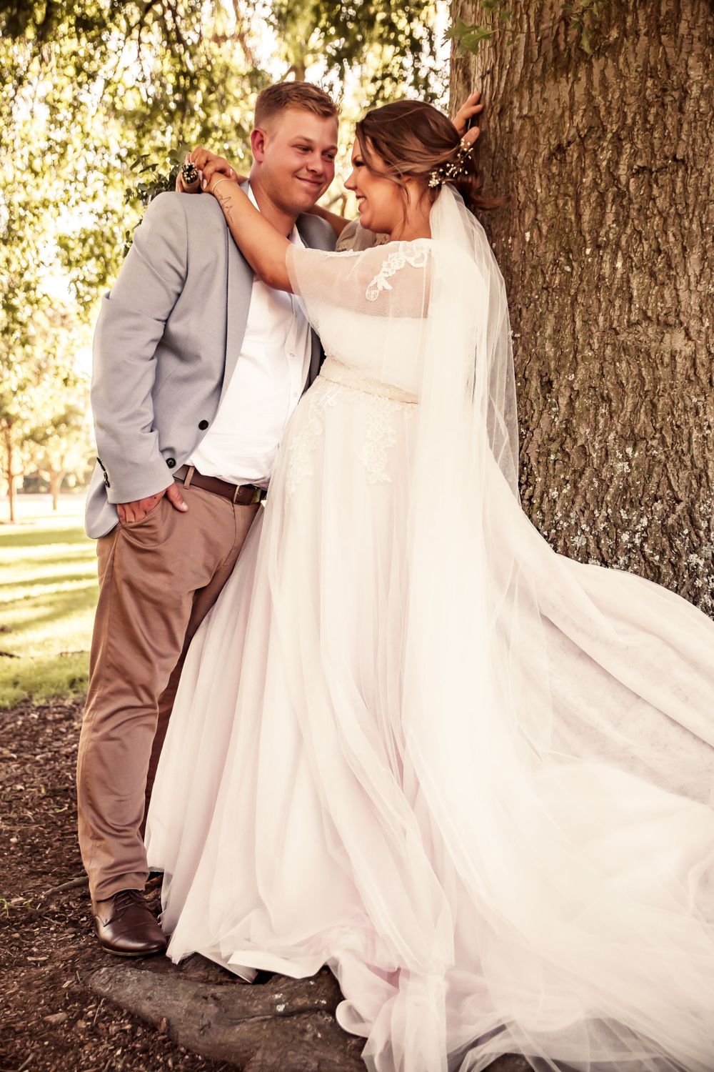 bride and groom leaning against large oak tree and laughing as they embrace