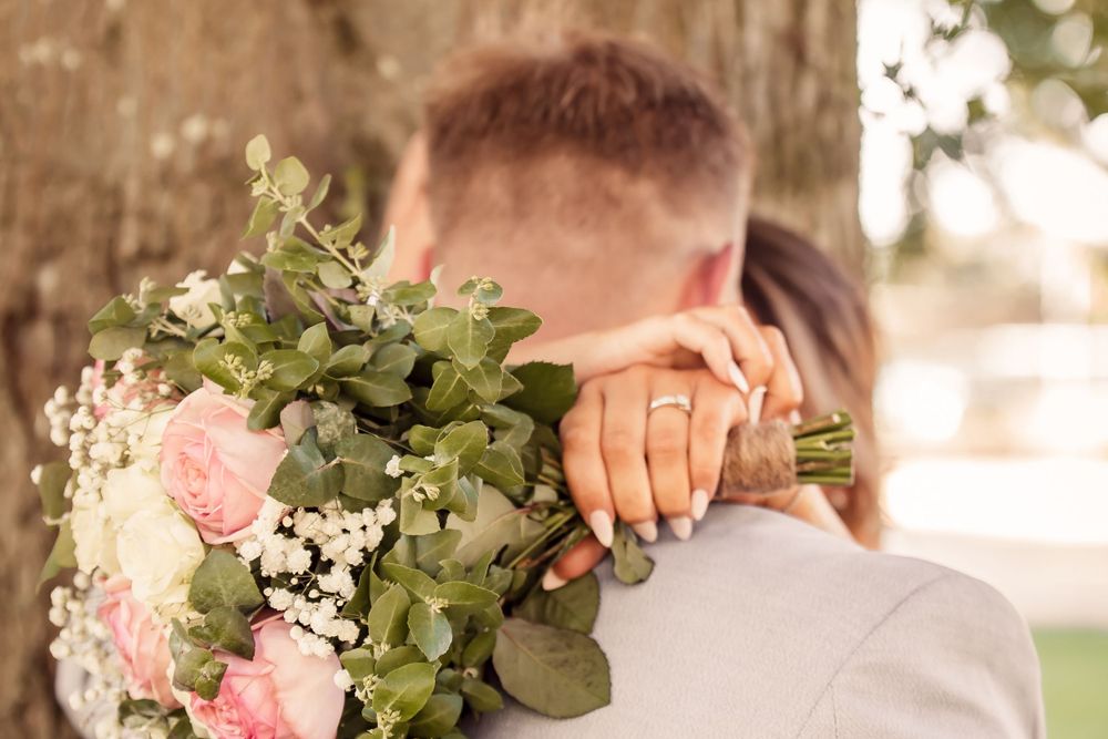 closeup of bouquet and ring with bride holding hands behind grooms neck
