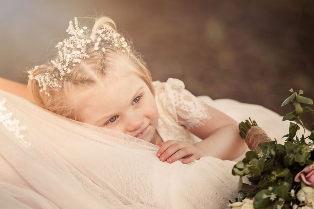 closeup of flowergirl laying on brides train her hair is braided and had babies breath woven through it