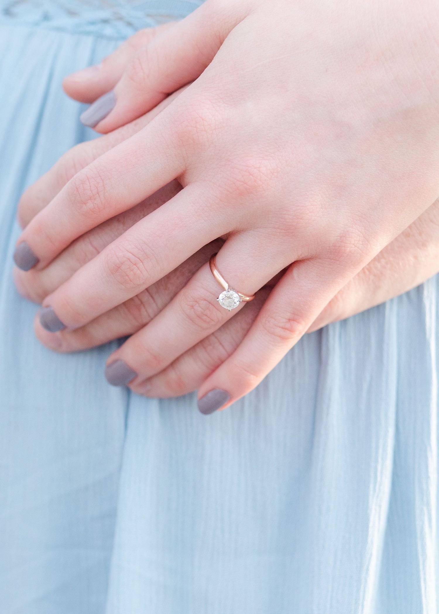 Close-up of hands wearing an engagement ring against light blue fabric.