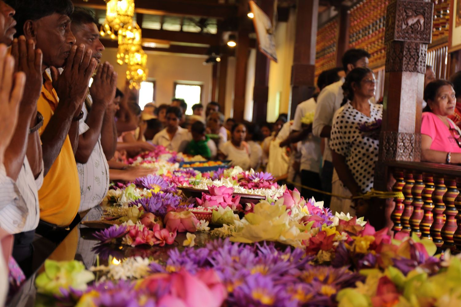 Colorful flower offerings and decorations at a busy temple gathering with devotees in attendance.