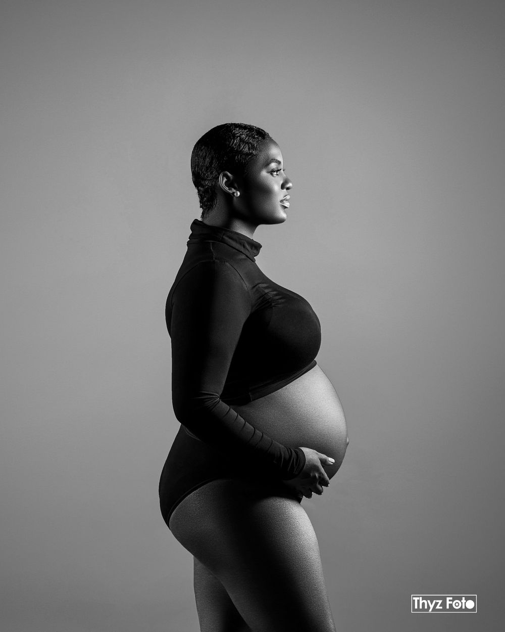 Dramatic black and white maternity portrait of a woman cradling her belly, showcasing the beauty of motherhood.