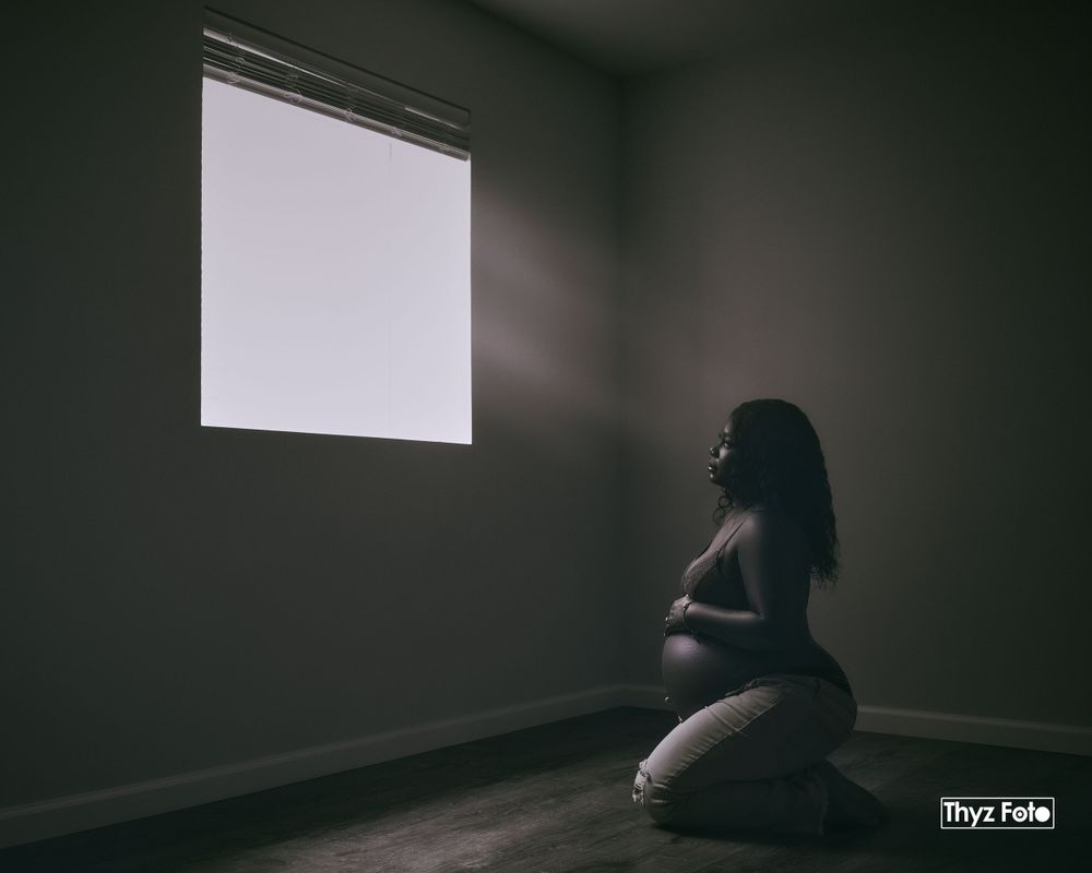 Artistic portrait of a woman sitting in a dimly lit room, evoking a moody and introspective atmosphere.