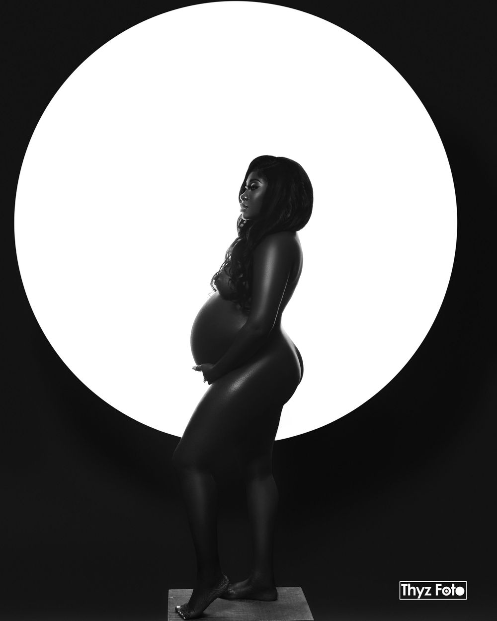 Silhouette maternity portrait of an expecting mother in a black dress, posed against a circular light background.