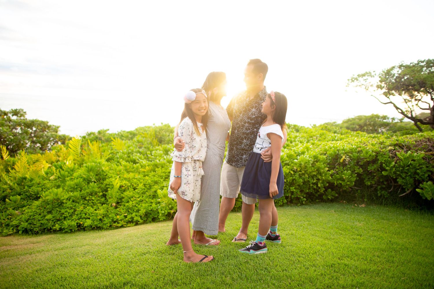 A group stands together on a lush green lawn backlit by warm golden sunlight during sunset.