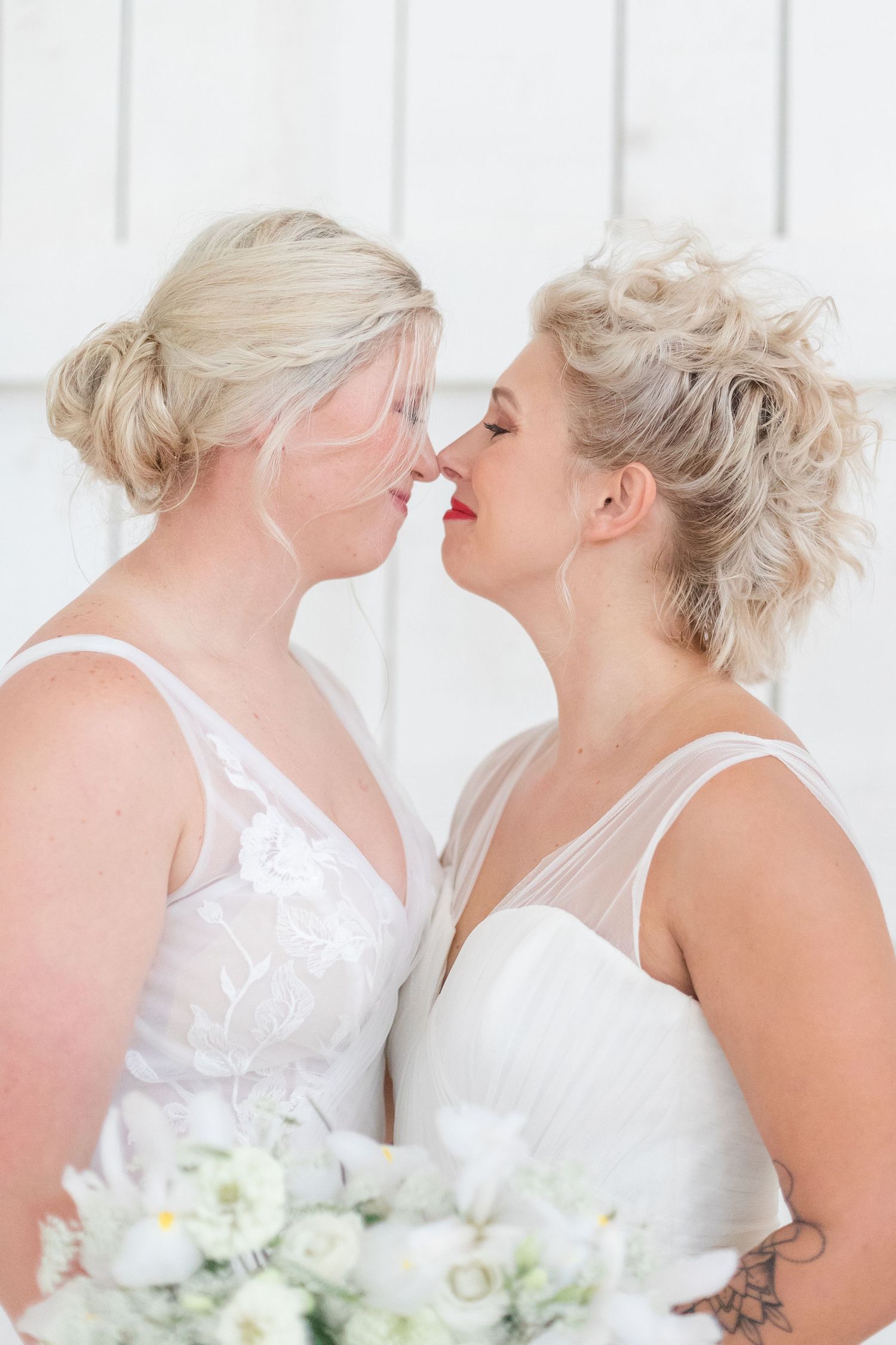 Two people in white wedding dresses sharing an intimate moment against a white backdrop.