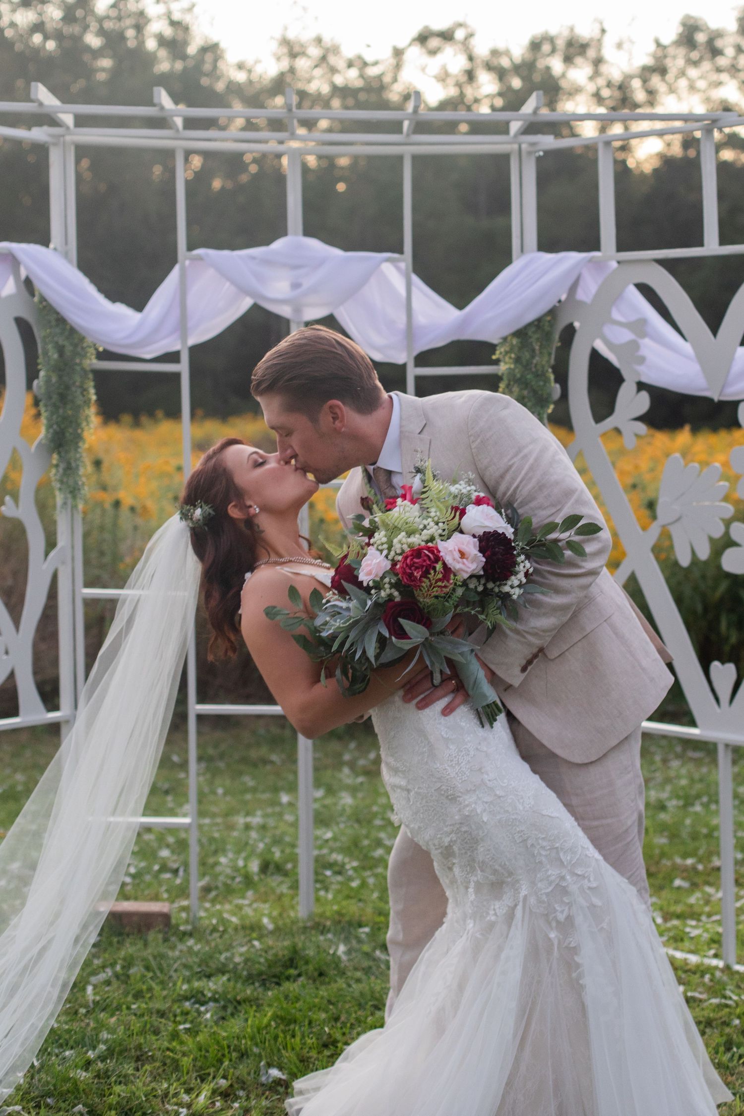 Romantic dip kiss between newlyweds in front of white decorative wedding backdrop.