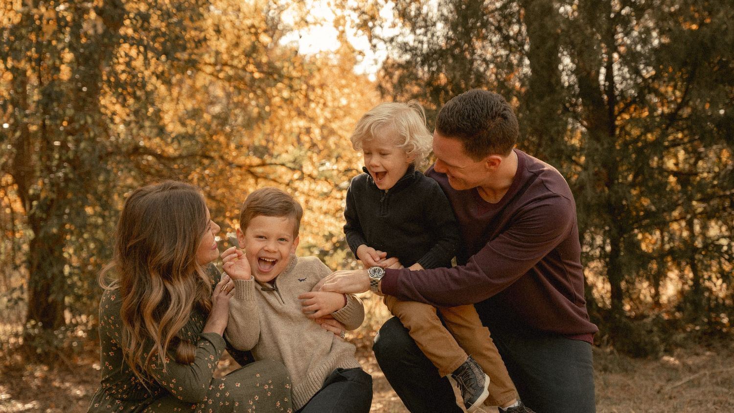 A loving family shares a playful moment together in an autumn forest setting during golden hour.