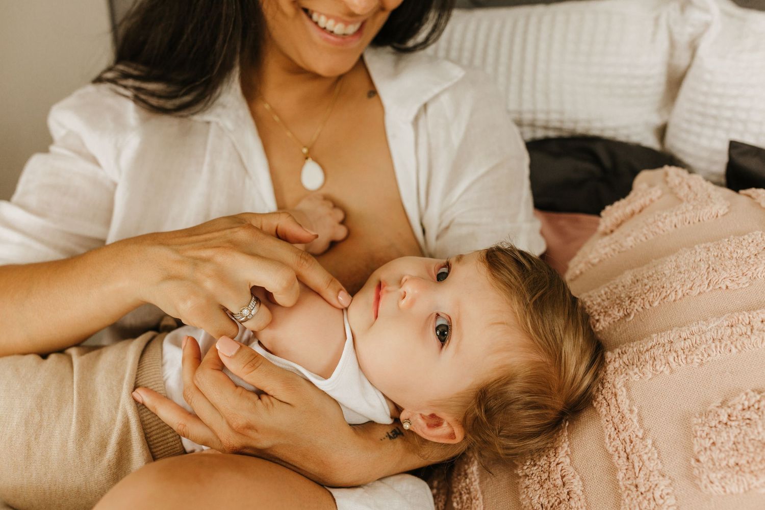 Tender moment between parent and baby while giving medicine or care on soft bedding.