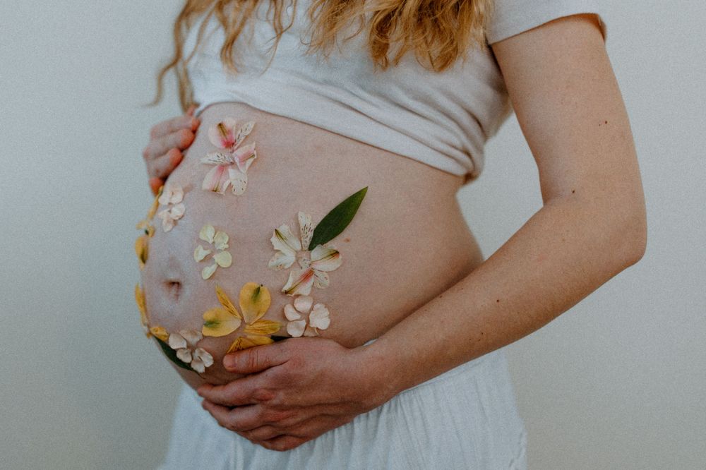 Pregnant belly decorated with delicate flowers against light background.