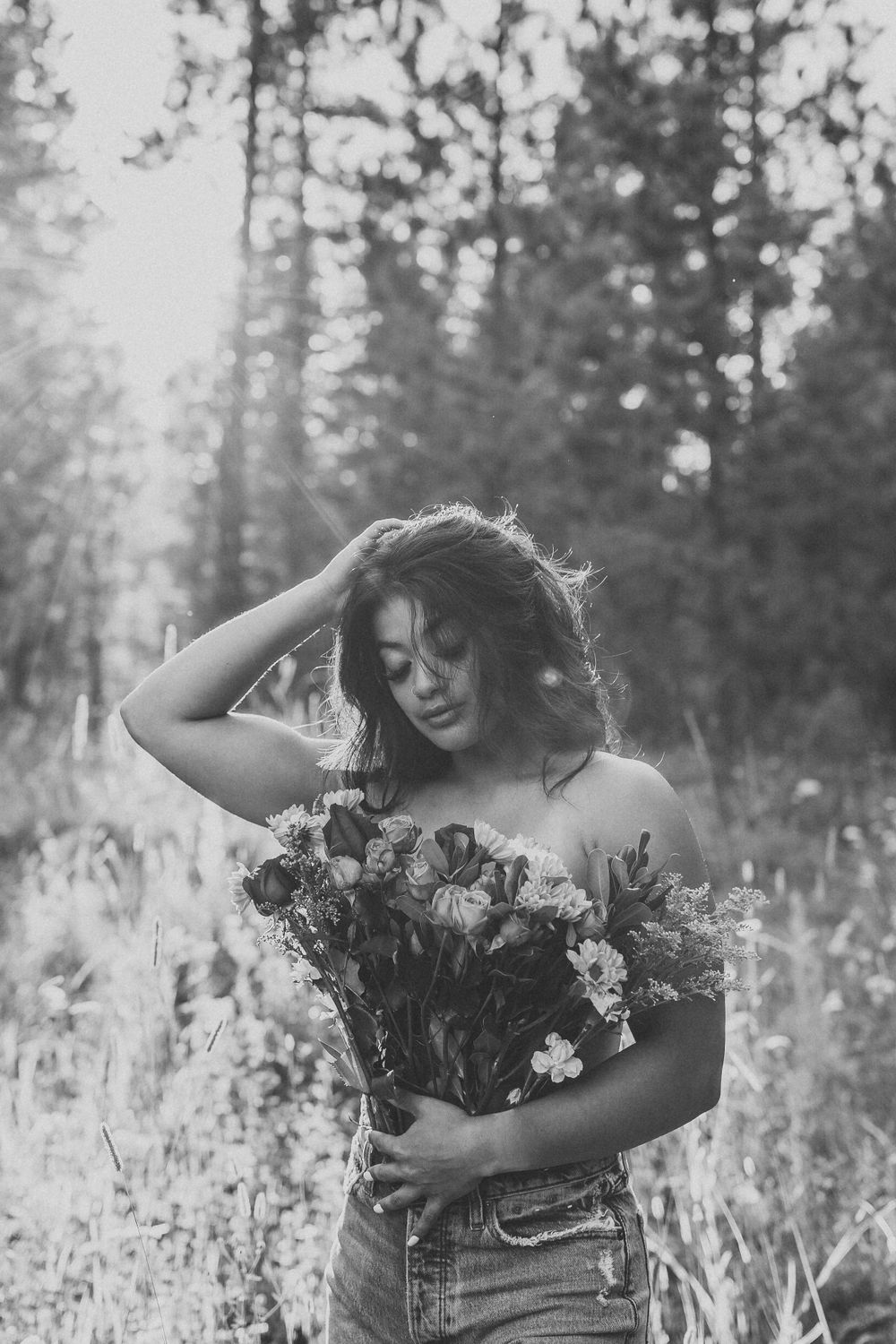 Woman holding wildflower bouquet in forest wearing denim.
